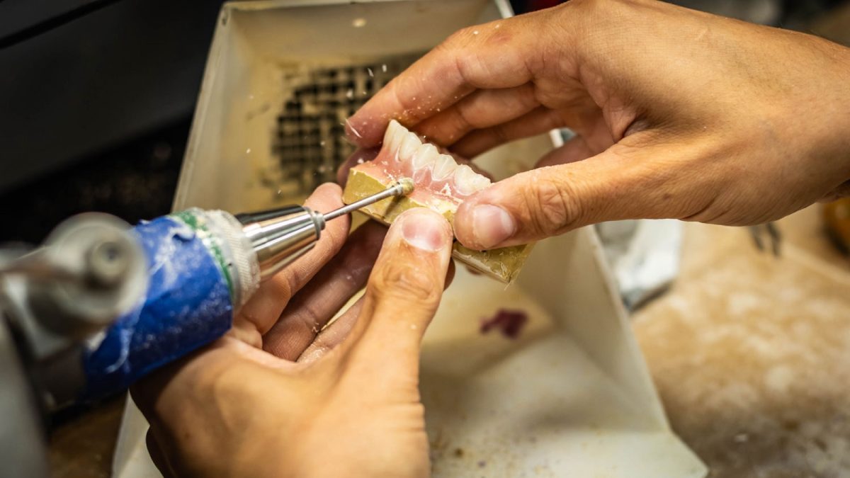 IDA technician finishing a denture base with a handpiece at the bench
