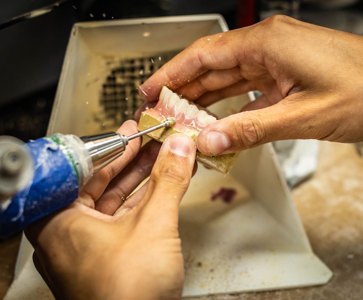 A technician finishing a denture base with a handpiece at the IDA bench