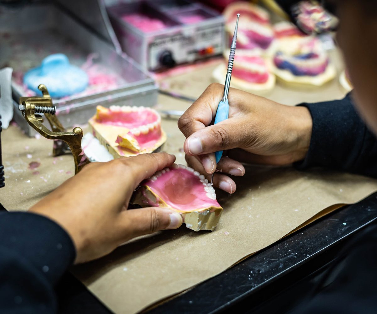 A technician setting denture teeth in wax at the IDA bench