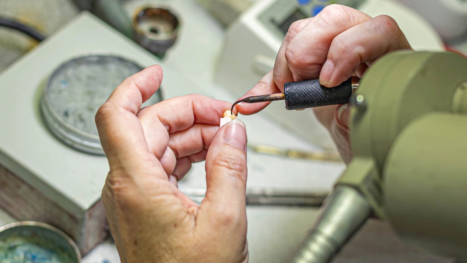 IDA technician shaping a ceramic crown with a handpiece at the Tulsa laboratory bench